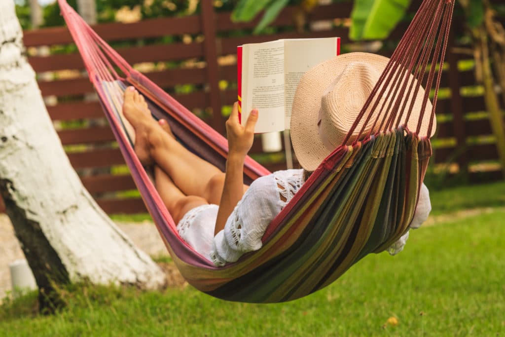 woman reading book in her yard hammock